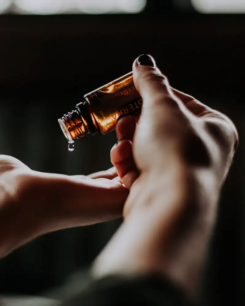 A drop of facial oil falling from a glass dropper into an open palm